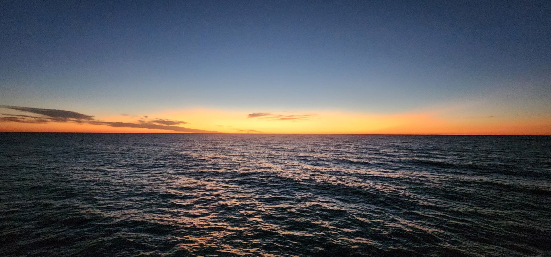 Sunset over a calm ocean, with orange and blue sky above dark rippling water.