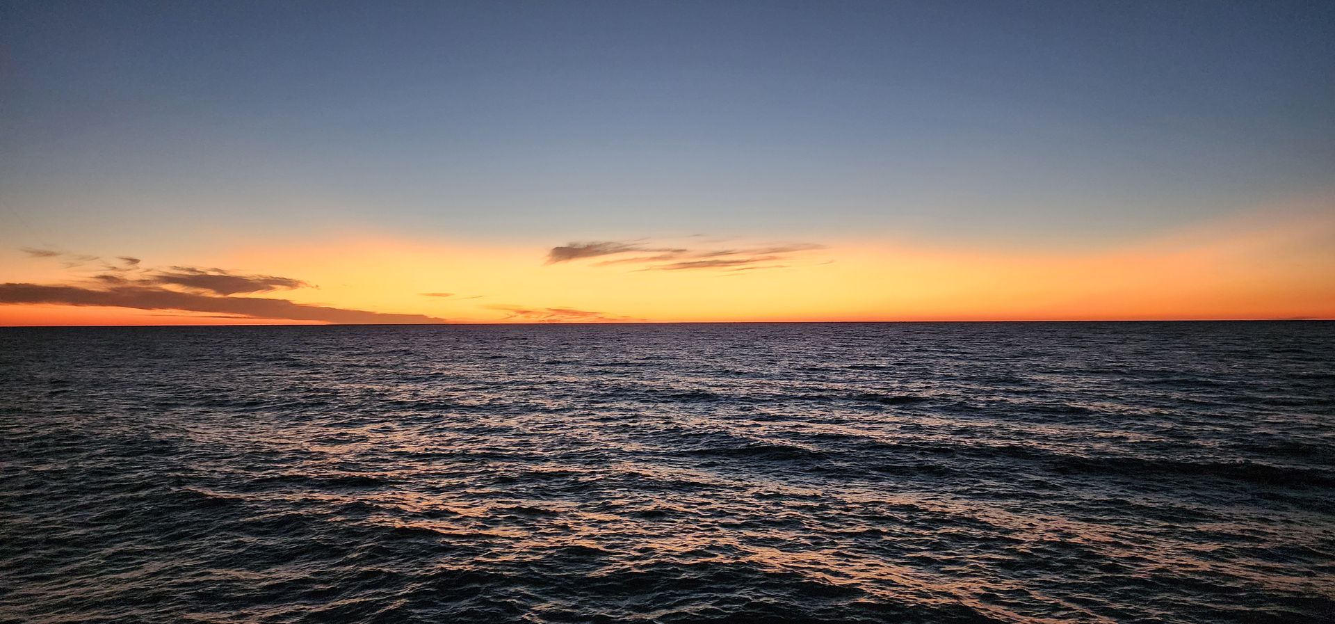 Sunset over a dark, rippling ocean with orange and pink sky above the horizon