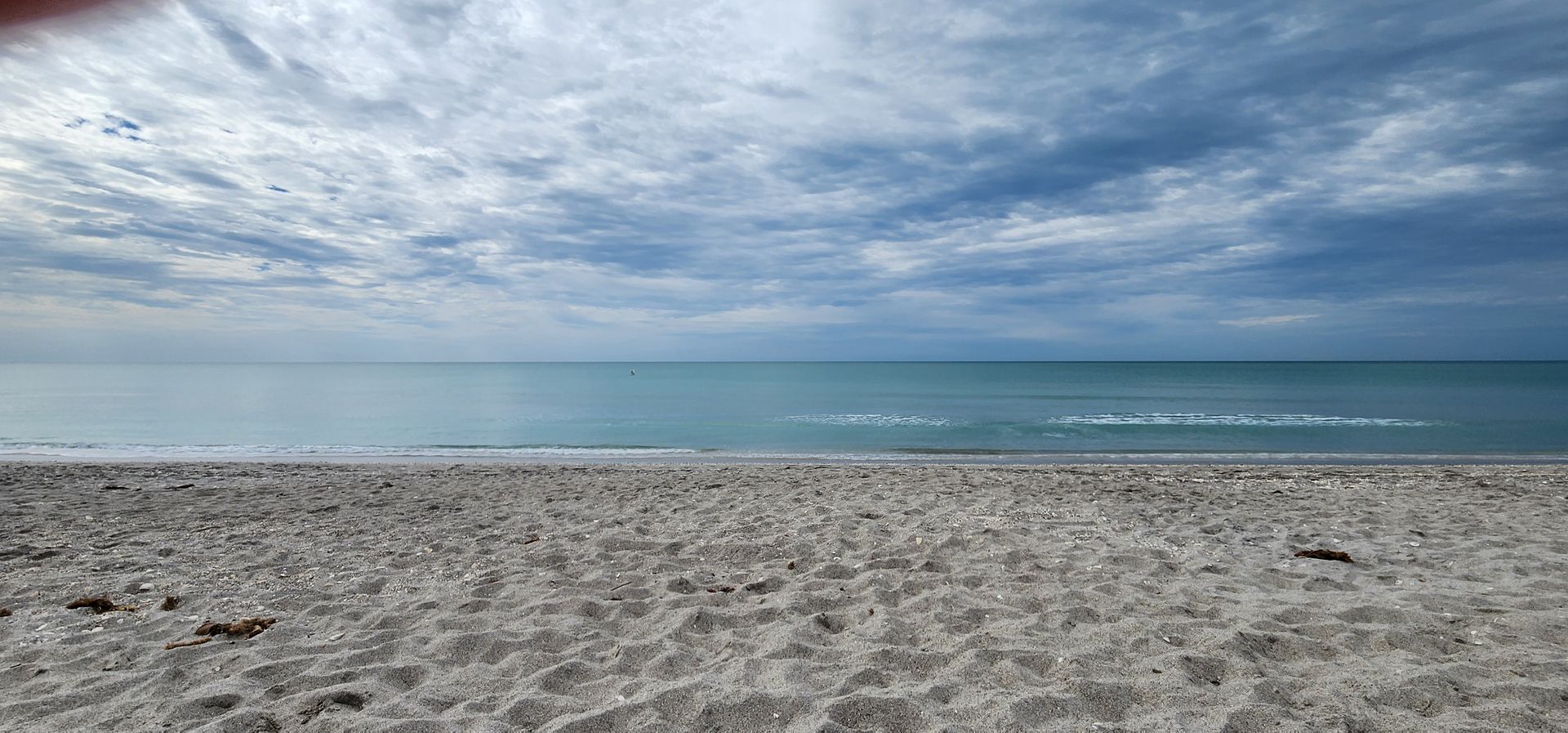 Empty sandy beach under a cloudy blue sky with calm ocean waves in the distance