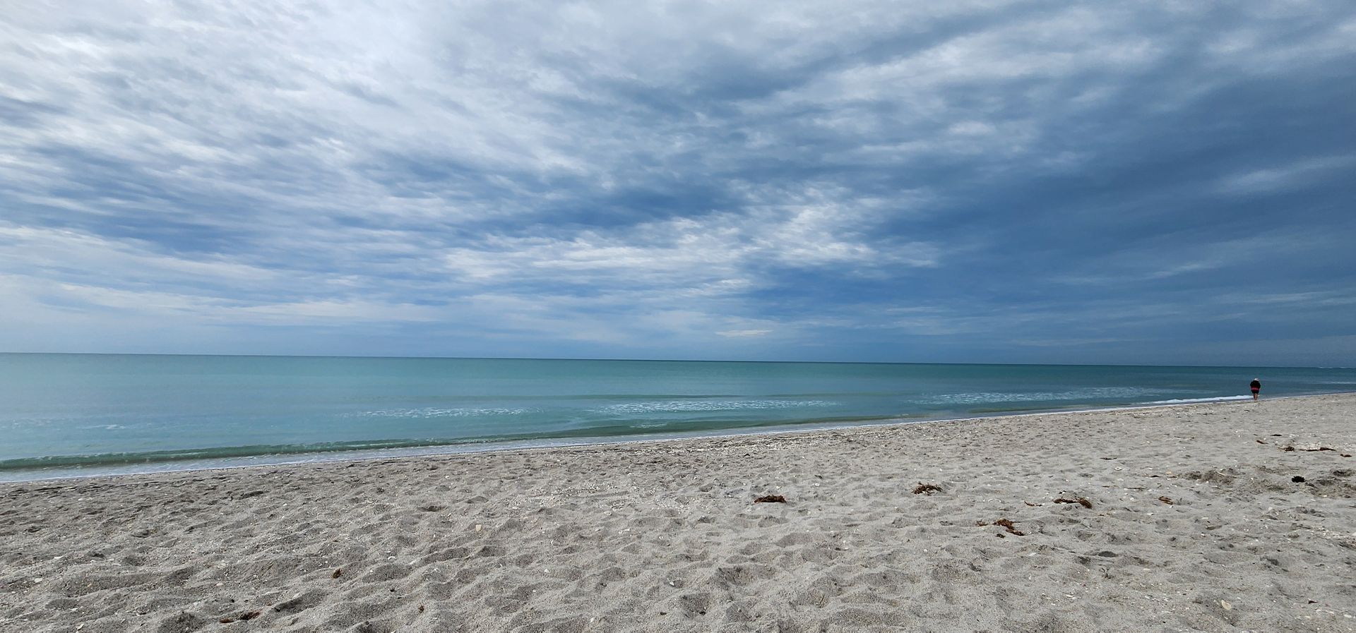 Wide sandy beach under a cloudy sky with calm blue water and a distant horizon