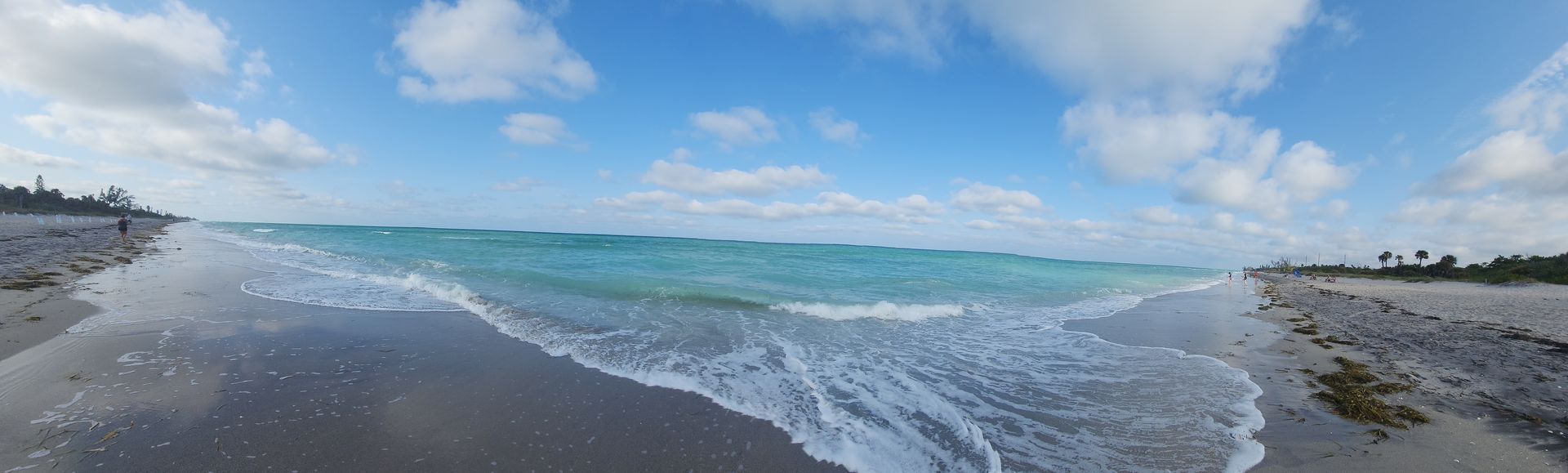 Wide sandy beach with gentle turquoise waves under a partly cloudy blue sky
