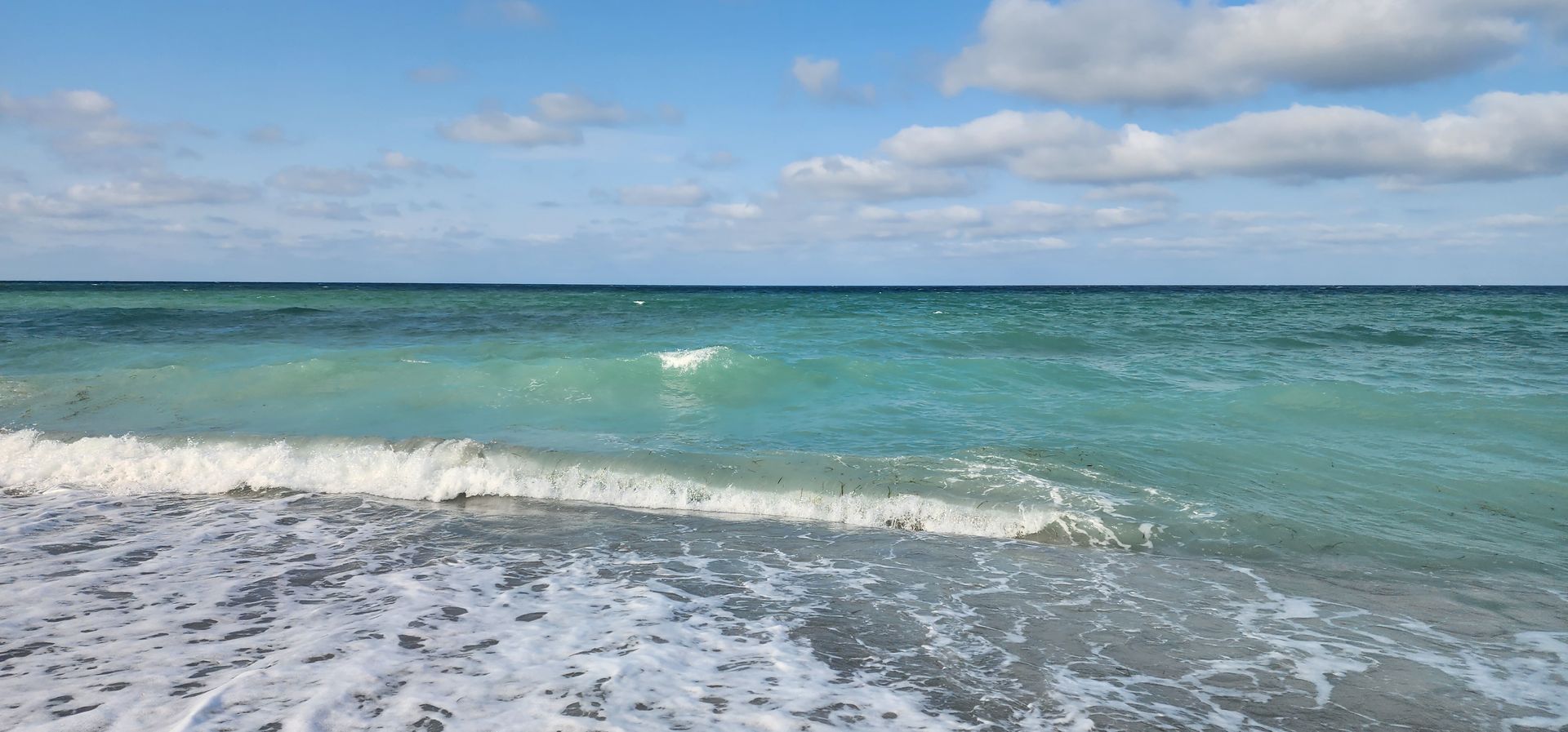 Turquoise ocean waves rolling onto a sandy beach under a blue sky