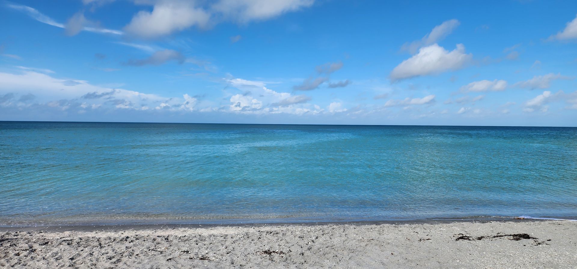 Calm turquoise ocean under a partly cloudy blue sky, with a rocky shoreline in the foreground