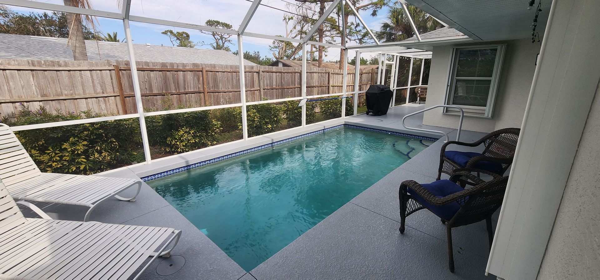 Screened-in patio with an in-ground pool, white lounge chair, and dark outdoor chairs under a covered lanai