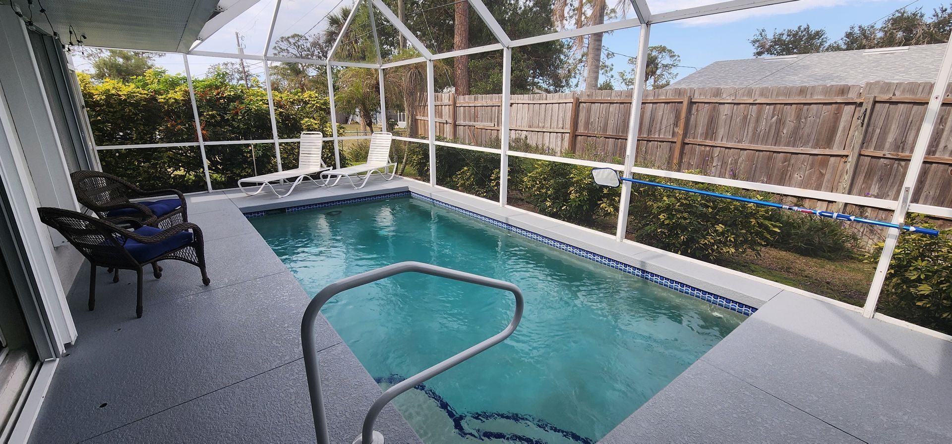 Screened backyard pool with turquoise water, white patio, and black chair beside the deck