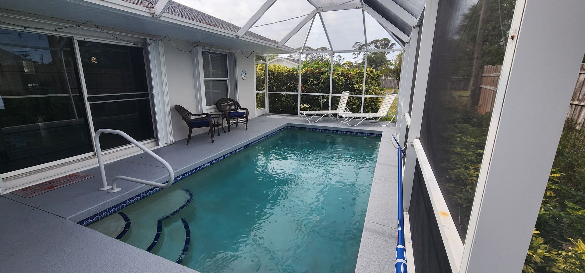 Covered patio with a rectangular swimming pool and lounge chairs beside large windows