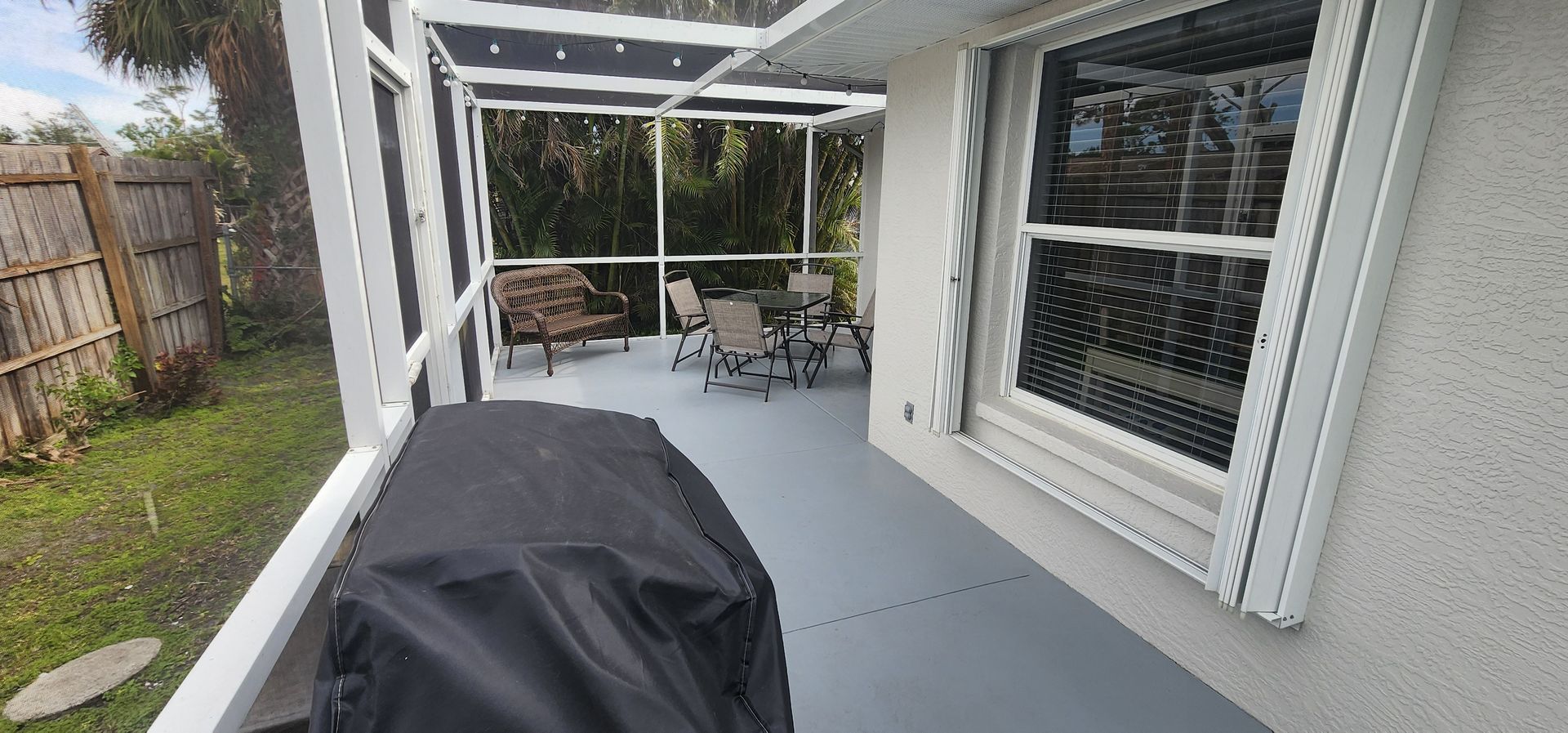 Covered patio with gray floor, black grill cover, and white-framed windows overlooking a fenced yard