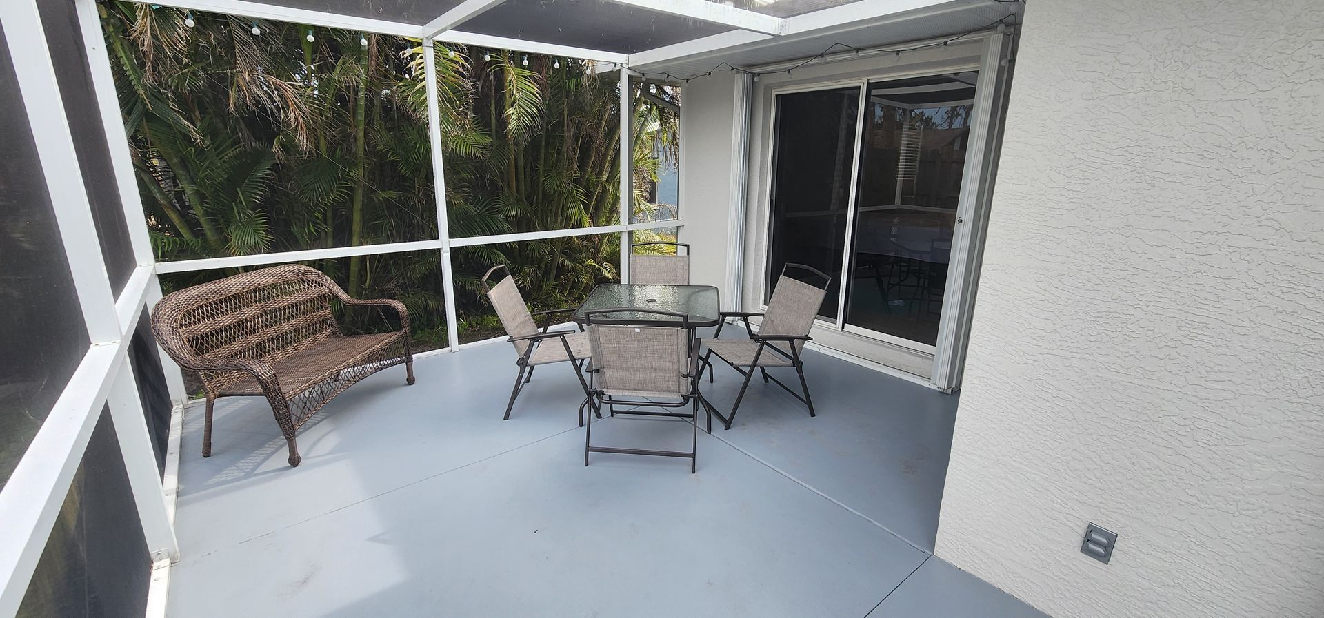 Covered patio with white mesh screens, wicker bench, and a small round table with chairs overlooking greenery