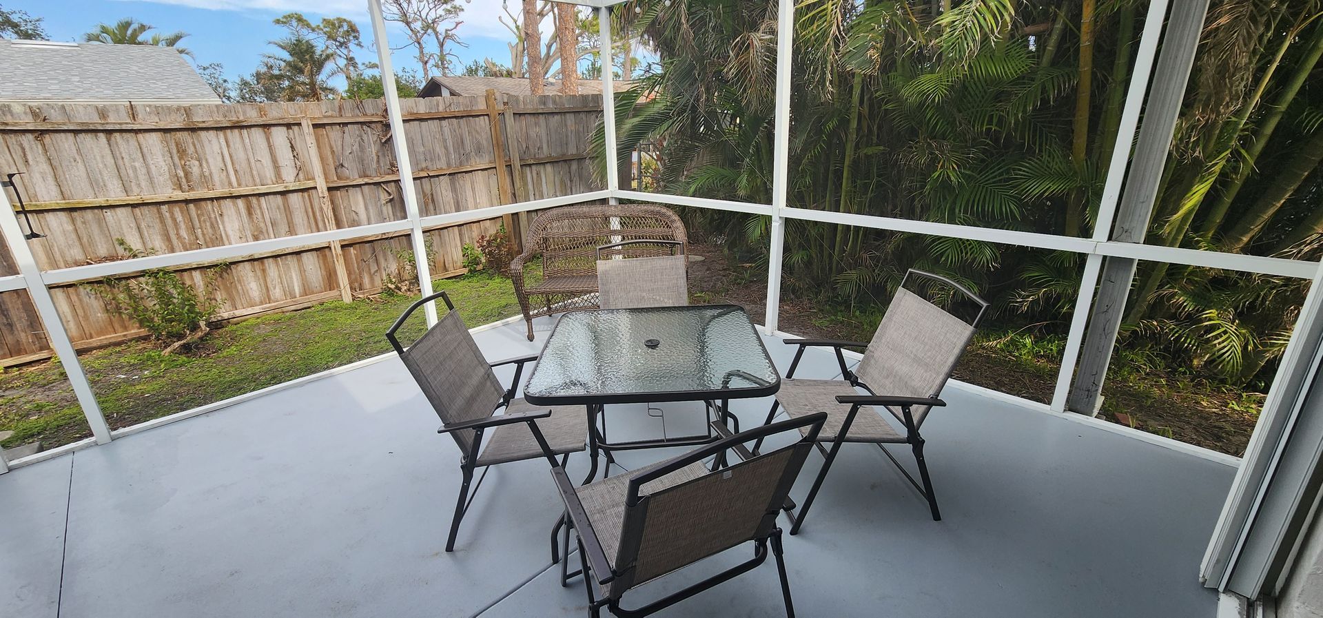 Covered patio with glass table, four chairs, and a wooded backyard view