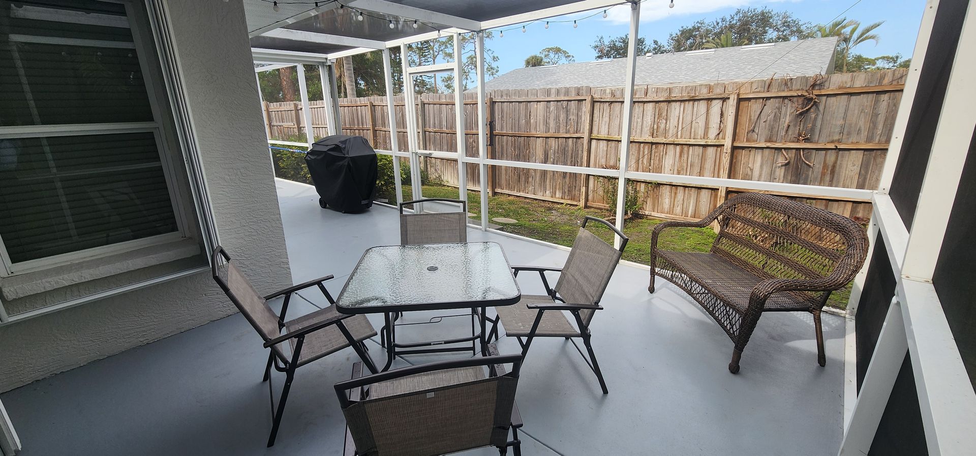 Covered patio with glass table and chairs, potted plants, and a fenced yard beyond.