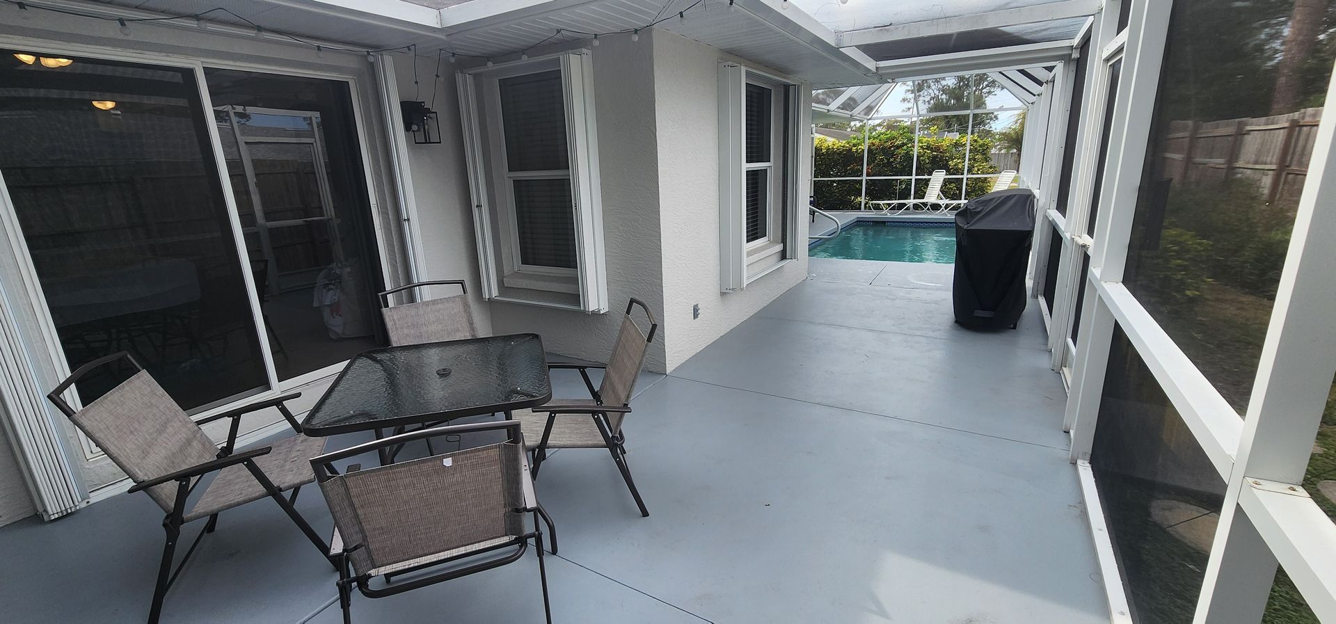 Covered patio with chairs, glass table, and screened windows along a house exterior
