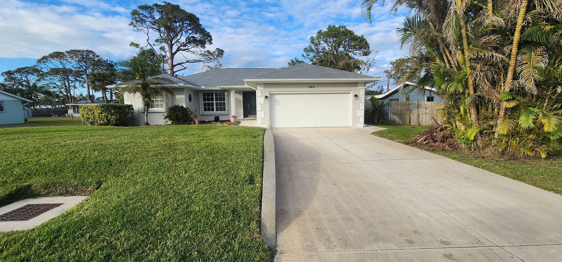 Single-story white house with a two-car garage, driveway, and green lawn under a blue sky