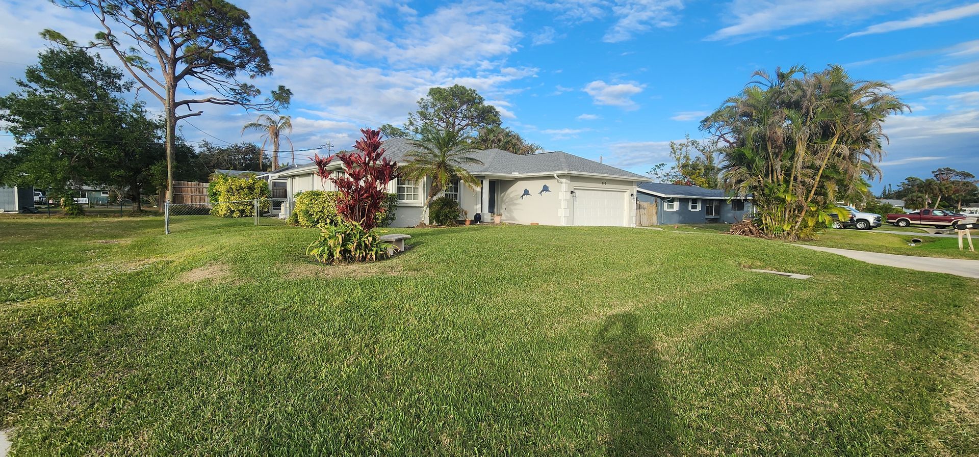 Suburban house with a wide green lawn, trees, and a partly cloudy sky
