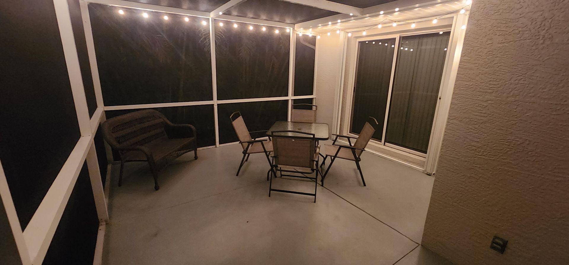 Covered patio with string lights, a table and chairs, and a bench at night