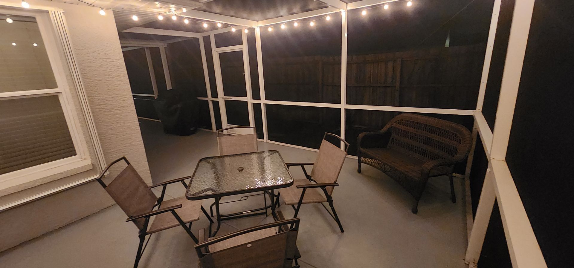 Screened-in patio with glass table, chairs, string lights, and a bench at night