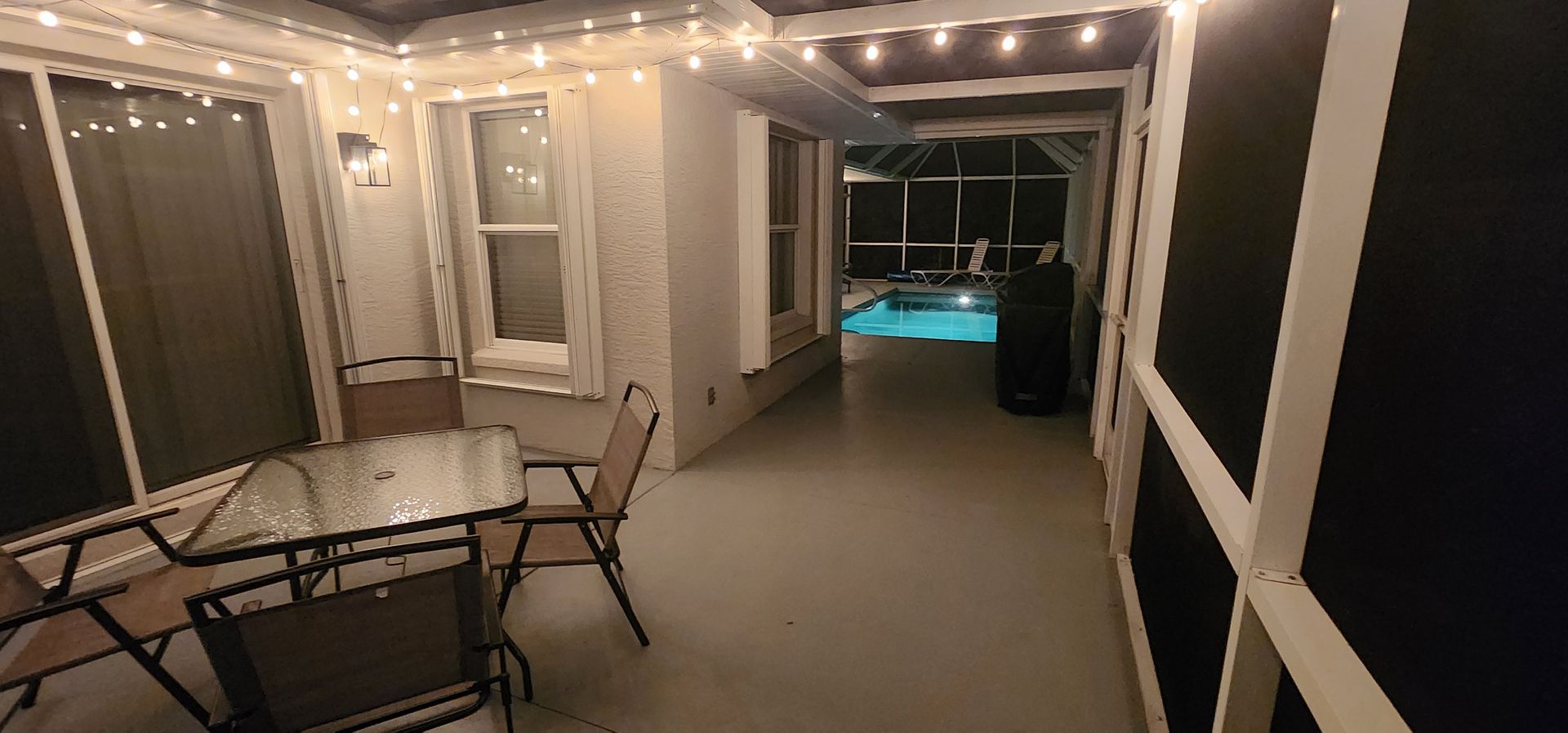 Covered patio with string lights, patio furniture, and a glowing pool at night