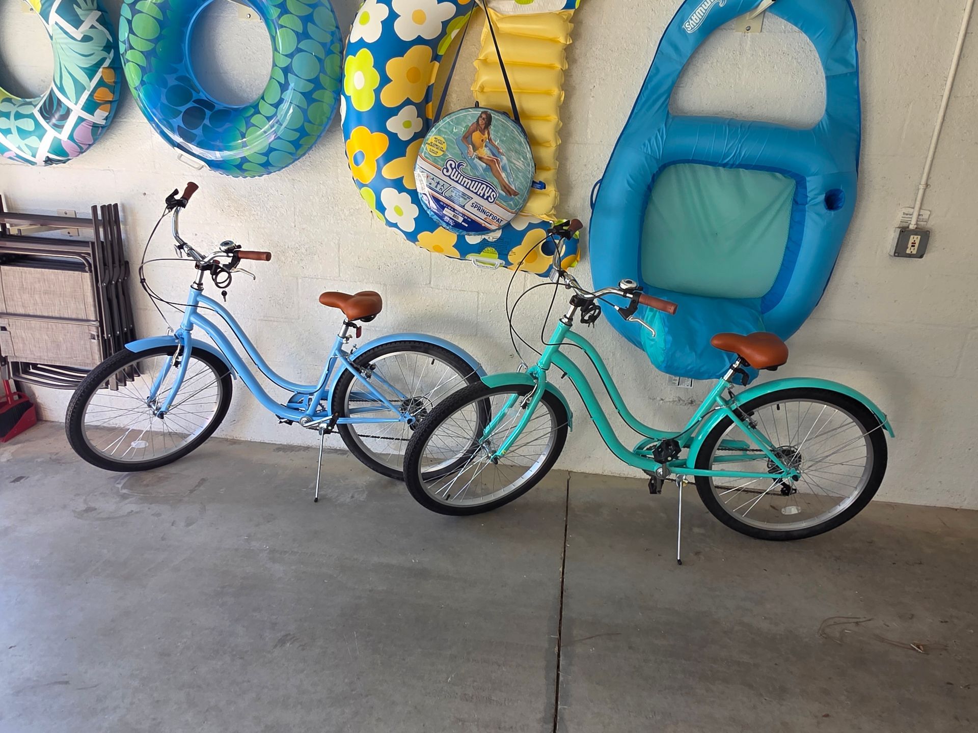 Two bicycles parked in a garage beside blue pool floats on the wall