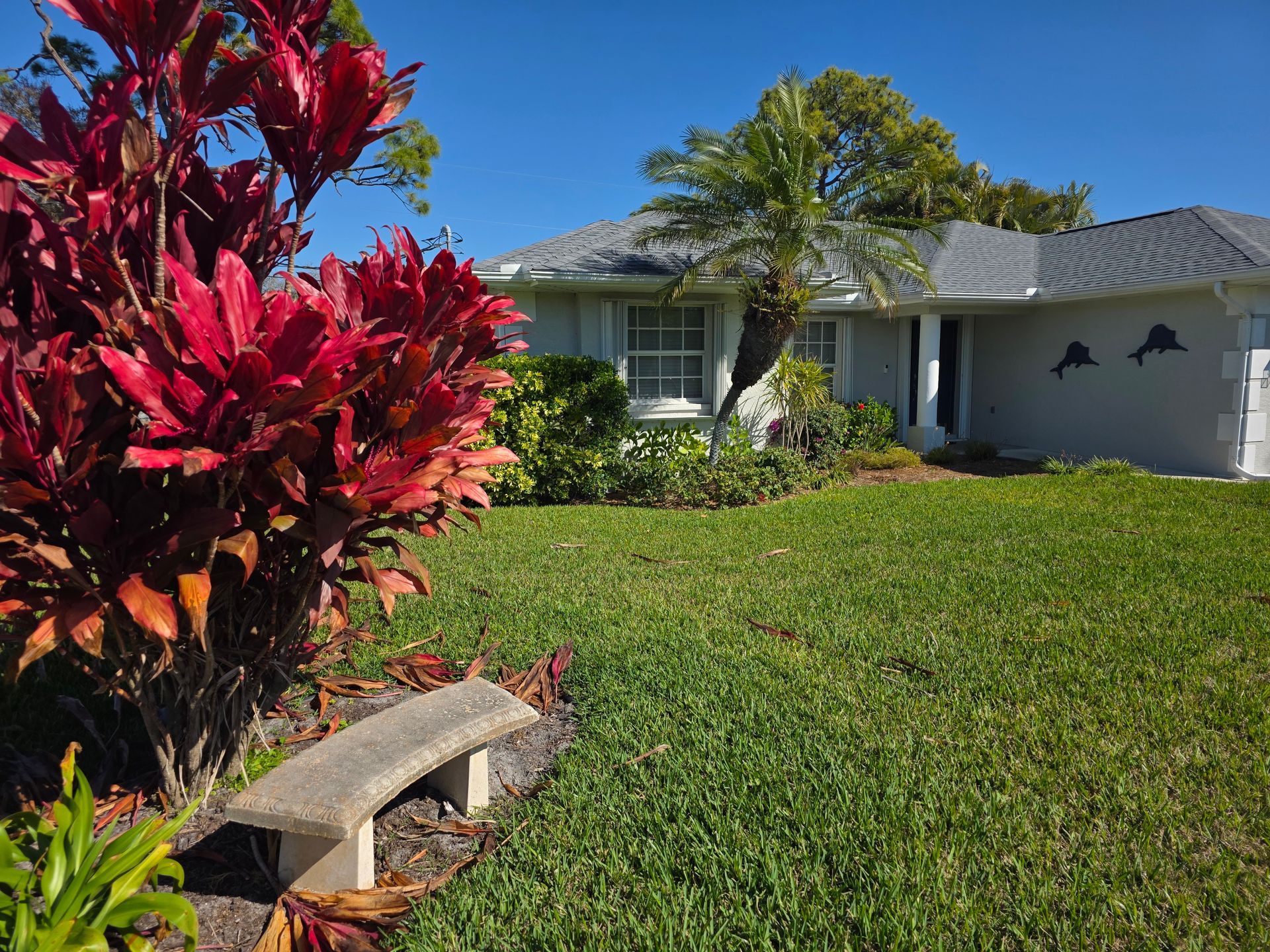 Suburban house with manicured lawn, red tropical plants, and a stone bench in the front yard