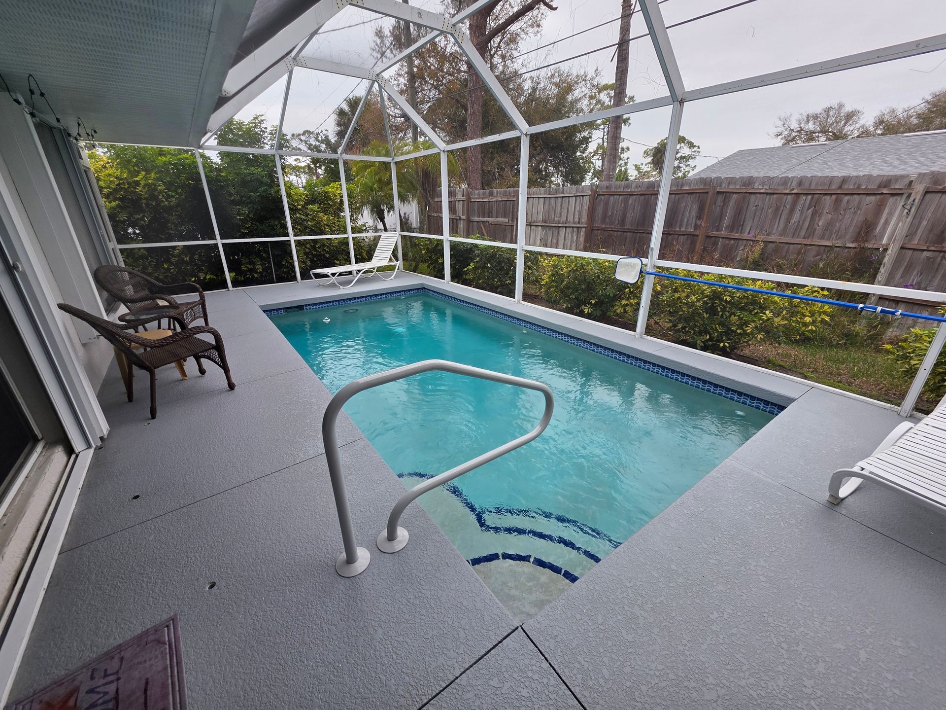 Screened backyard pool with turquoise water, white enclosure, and a covered chair on the deck