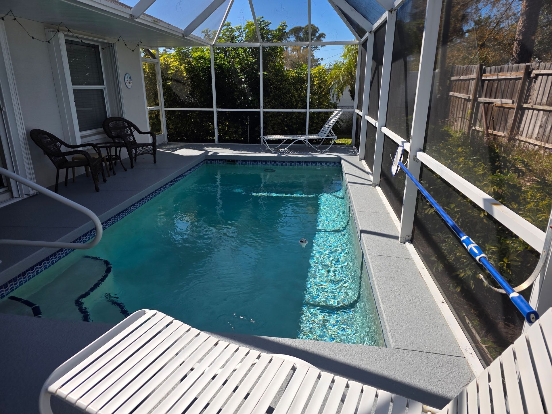 Screened-in backyard pool with white railings, turquoise water, and lounge chairs in sunlight