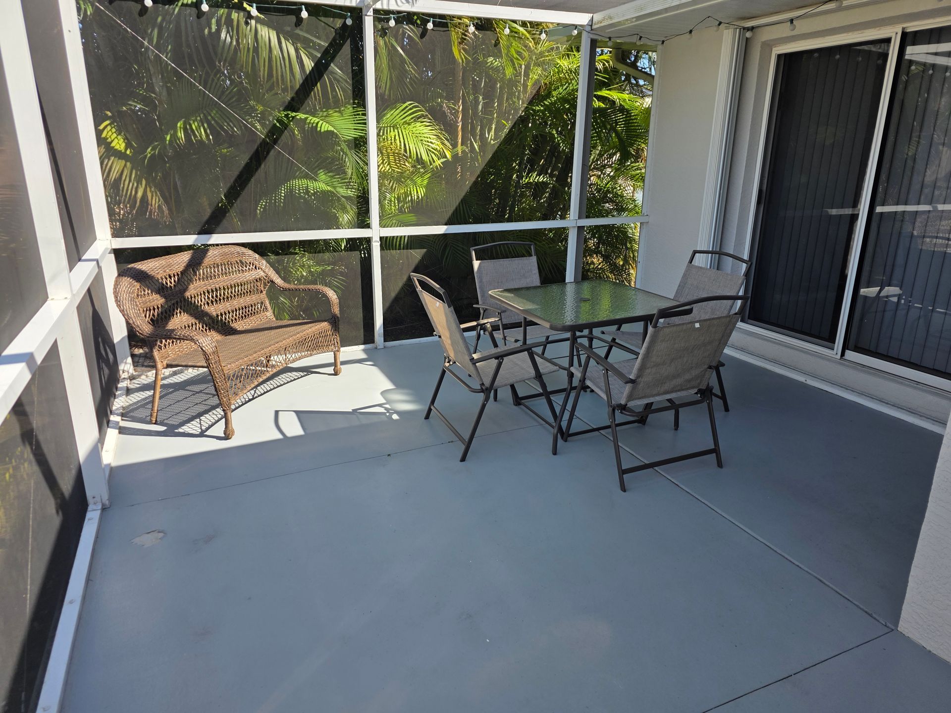Covered patio with gray floor, wicker chair, and glass table beside a screened wall and sliding door