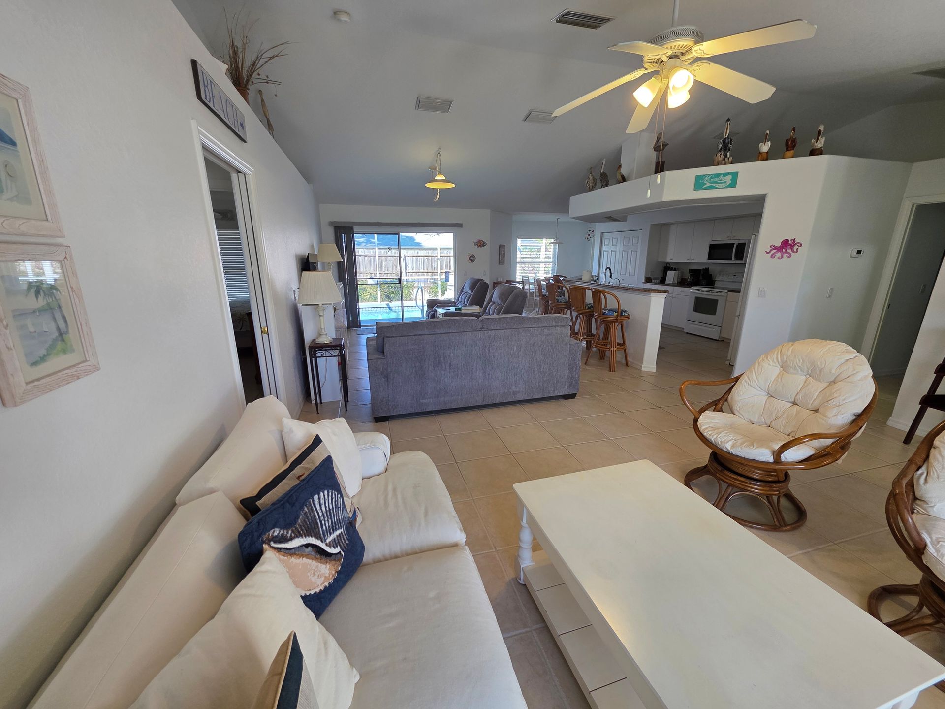 Bright living room with white sofa, coffee table, ceiling fans, and open kitchen area.