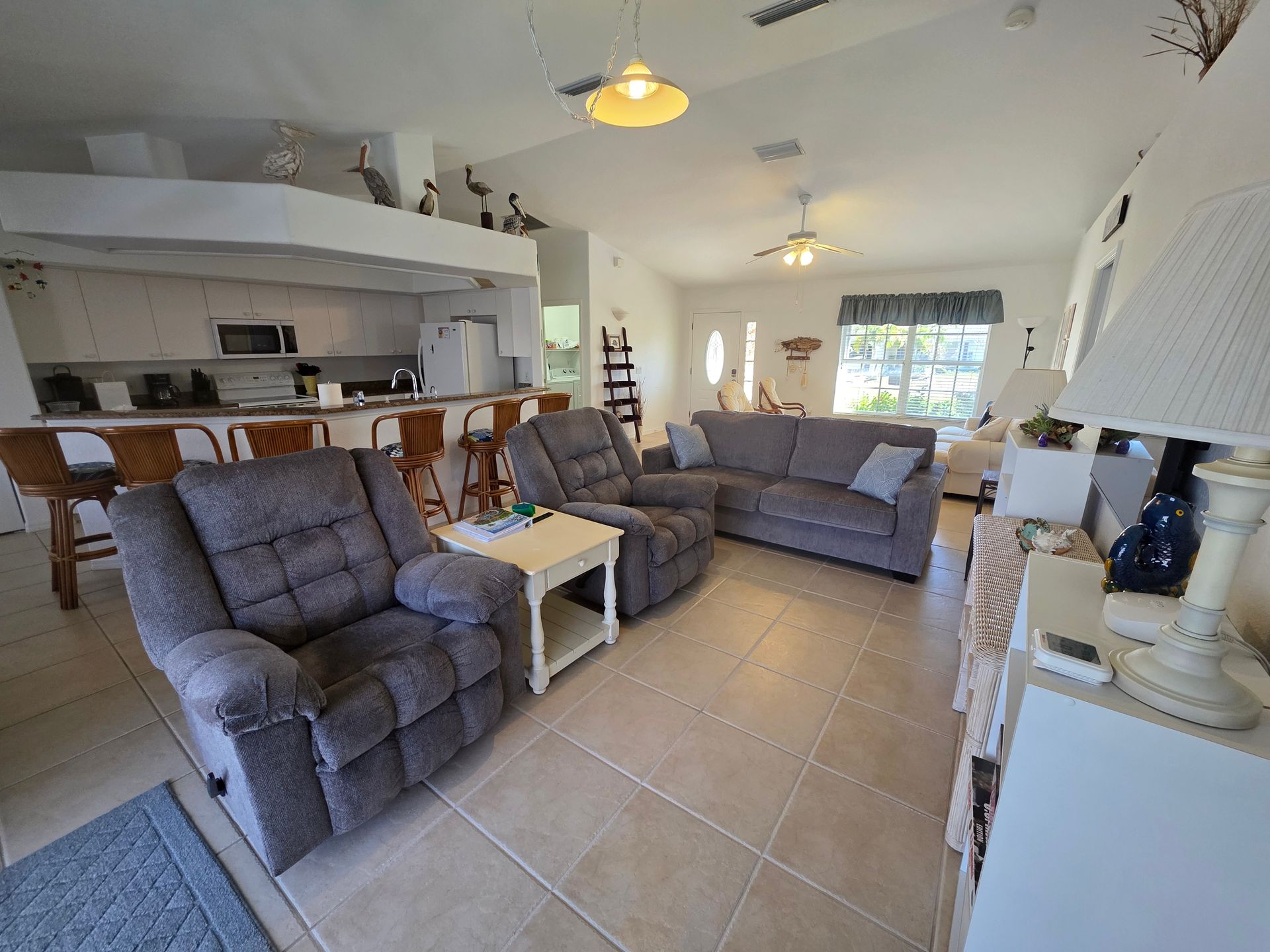 Living room with gray sofas, recliners, tiled floor, and bright windows