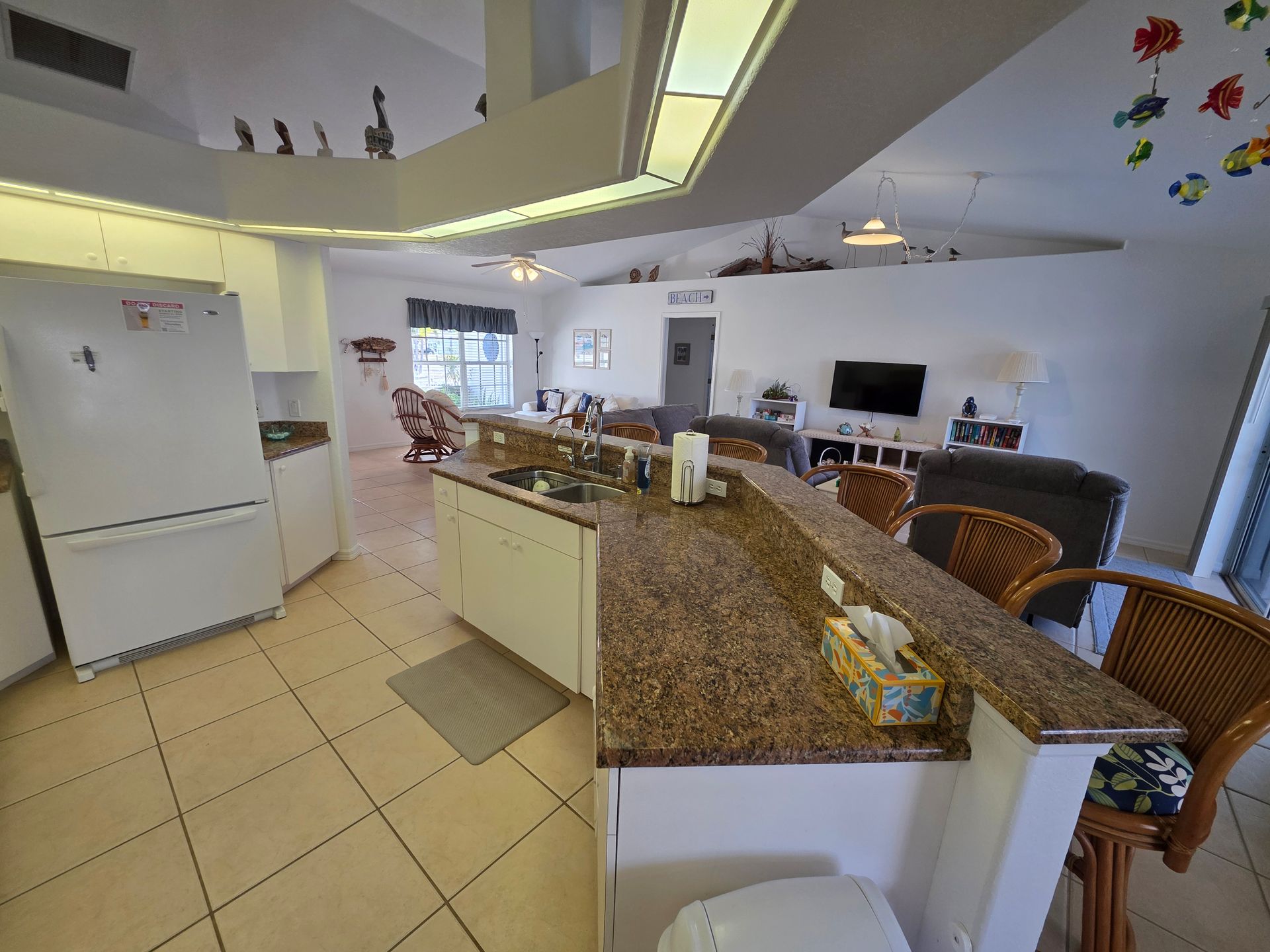 Bright kitchen with granite island, bar stools, white appliances, and tiled floor in a modern open-plan home