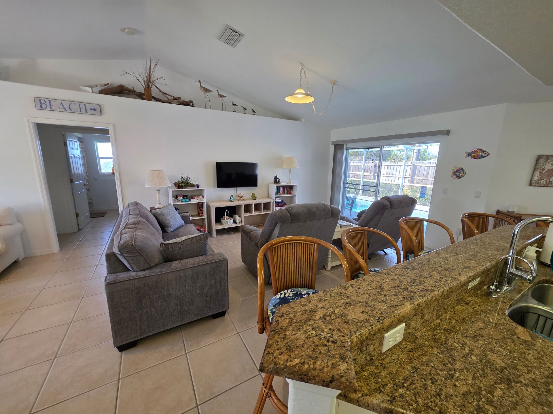 Open-plan living room and kitchen with gray sofa, wicker chairs, TV, and granite countertop.