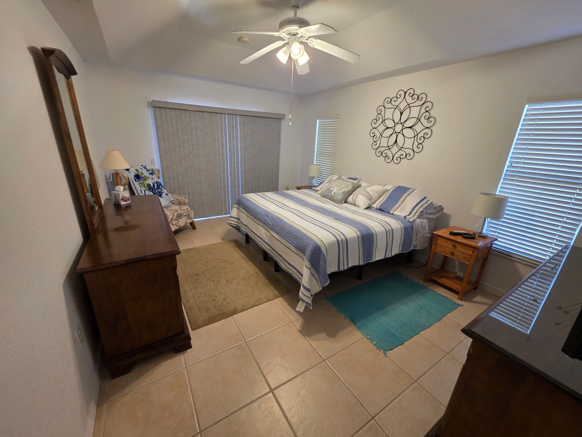 Bedroom with a bed, dresser, nightstands, ceiling fan, and windows with blinds.