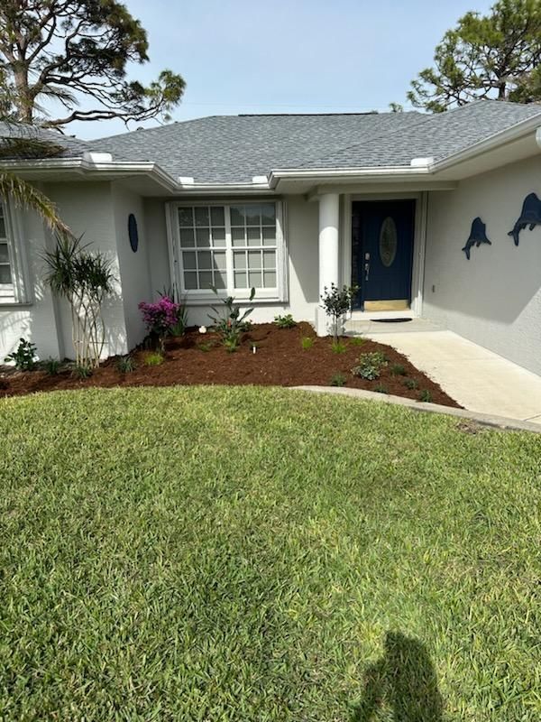 Single-story house with blue door, white shutters, front lawn, and landscaped flower bed.