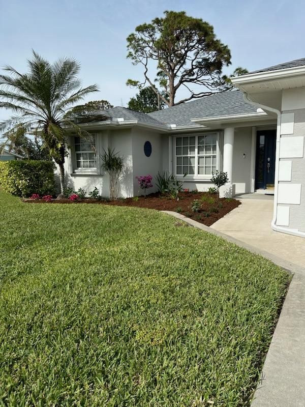 Single-story white house with a green lawn, palm trees, and a front walkway under clear daylight