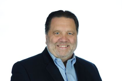 Headshot of a smiling man in a dark jacket and light blue shirt against a white background Headshot of a smiling man in a dark jacket and light blue shirt against a white background