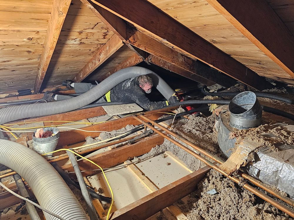 A man is working in an attic with a vacuum hose.