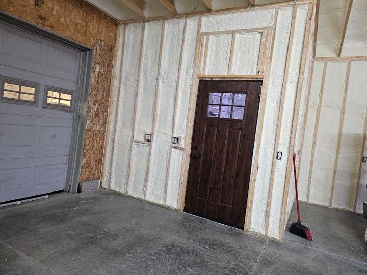 A man is standing on a ladder spraying insulation on a wall.