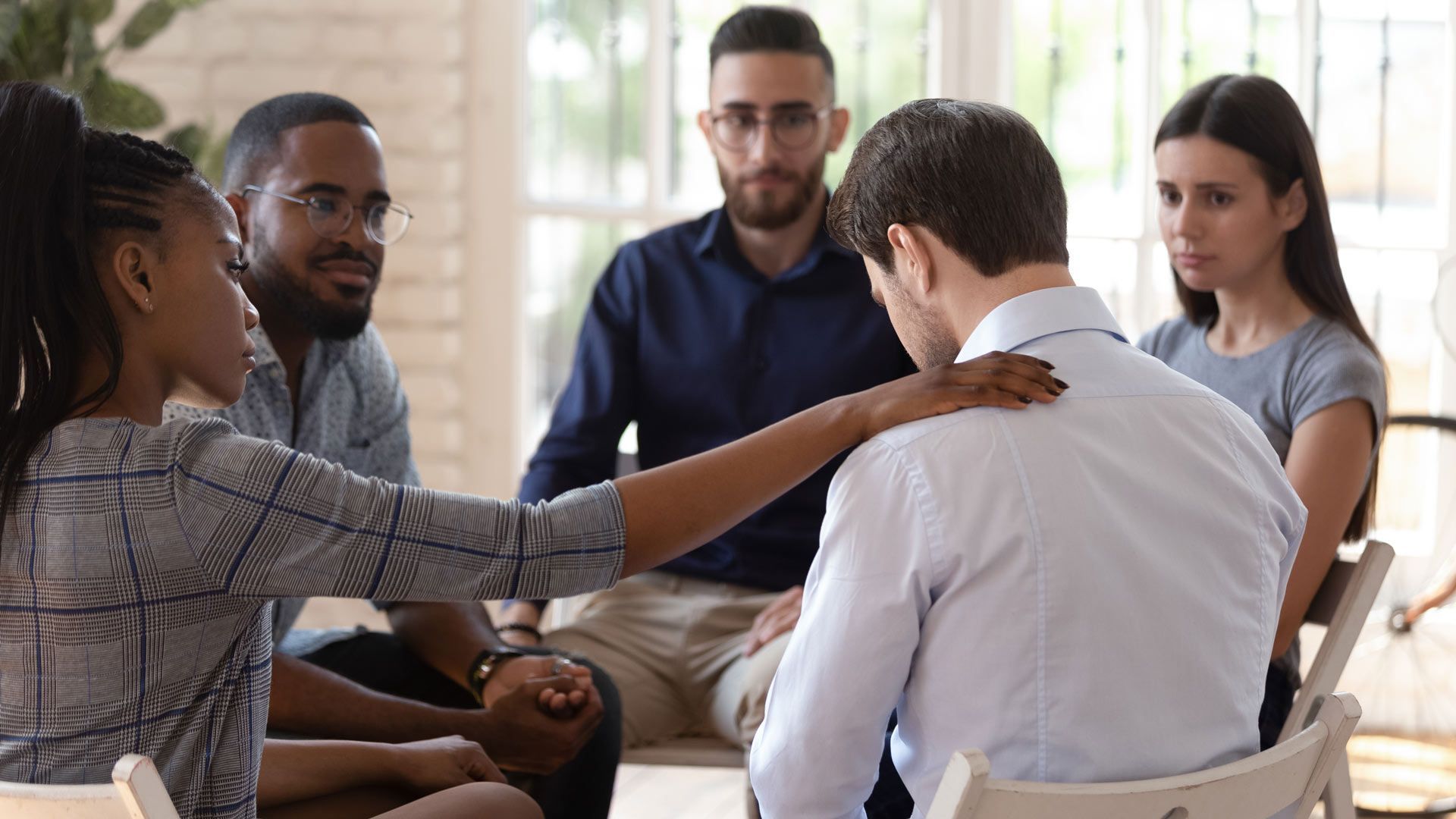 a group of people are sitting in a circle with a woman putting her hand on a man 's shoulder