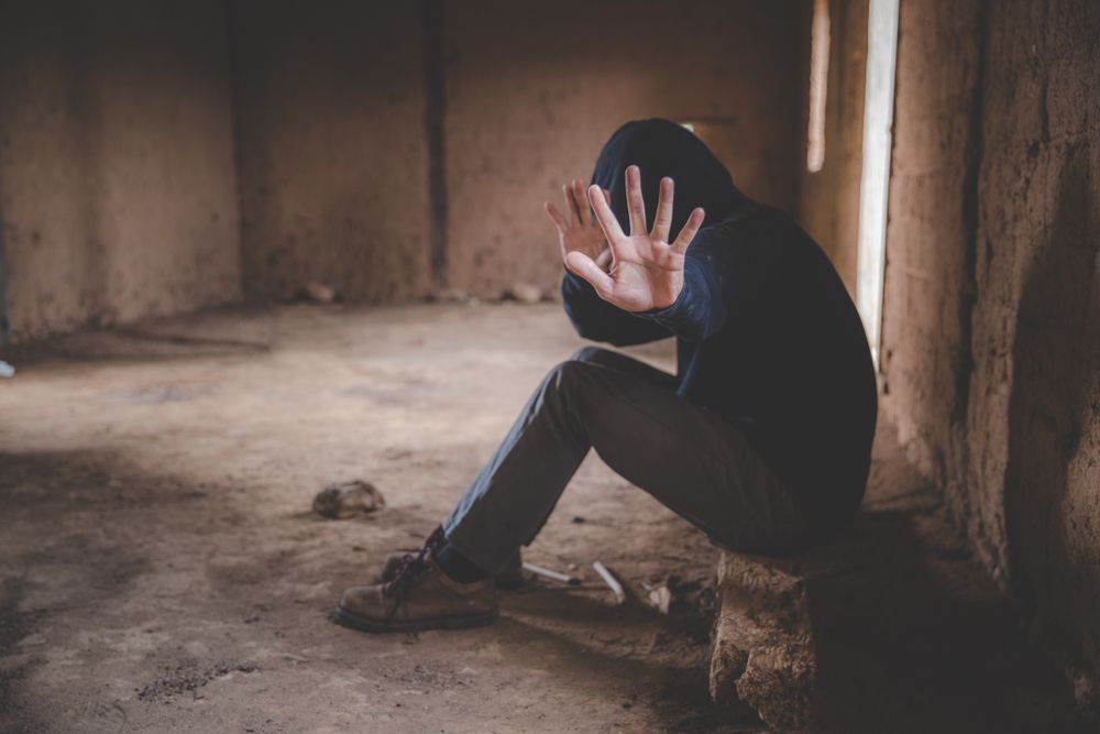 a man in a hooded jacket is sitting in a dark room with his hands covering his face