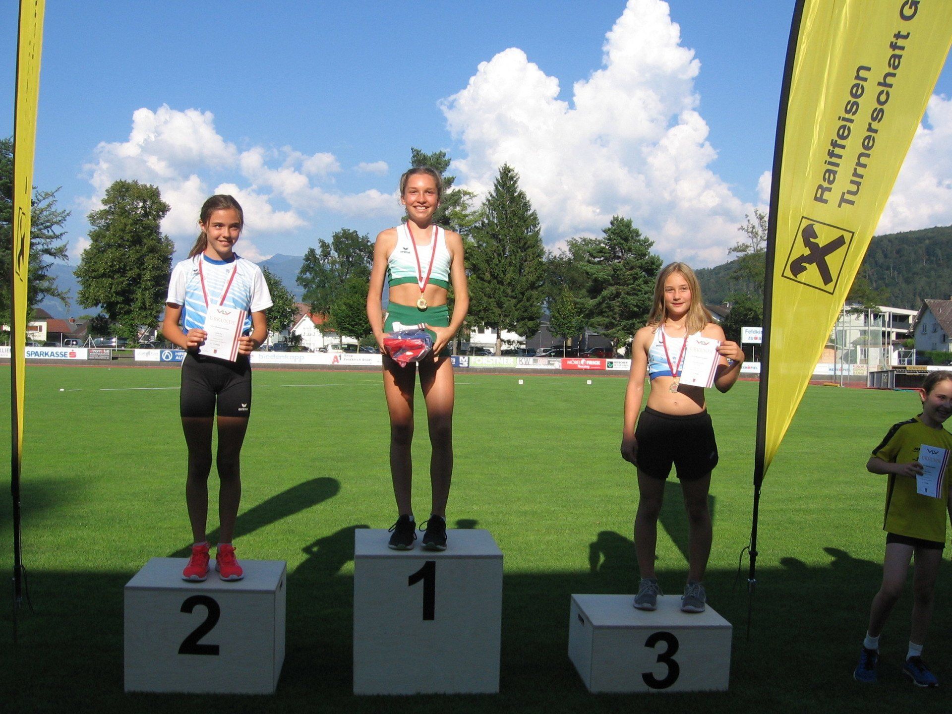 Drei Mädchen stehen auf einem Podium mit den Nummern 1, 2 und 3