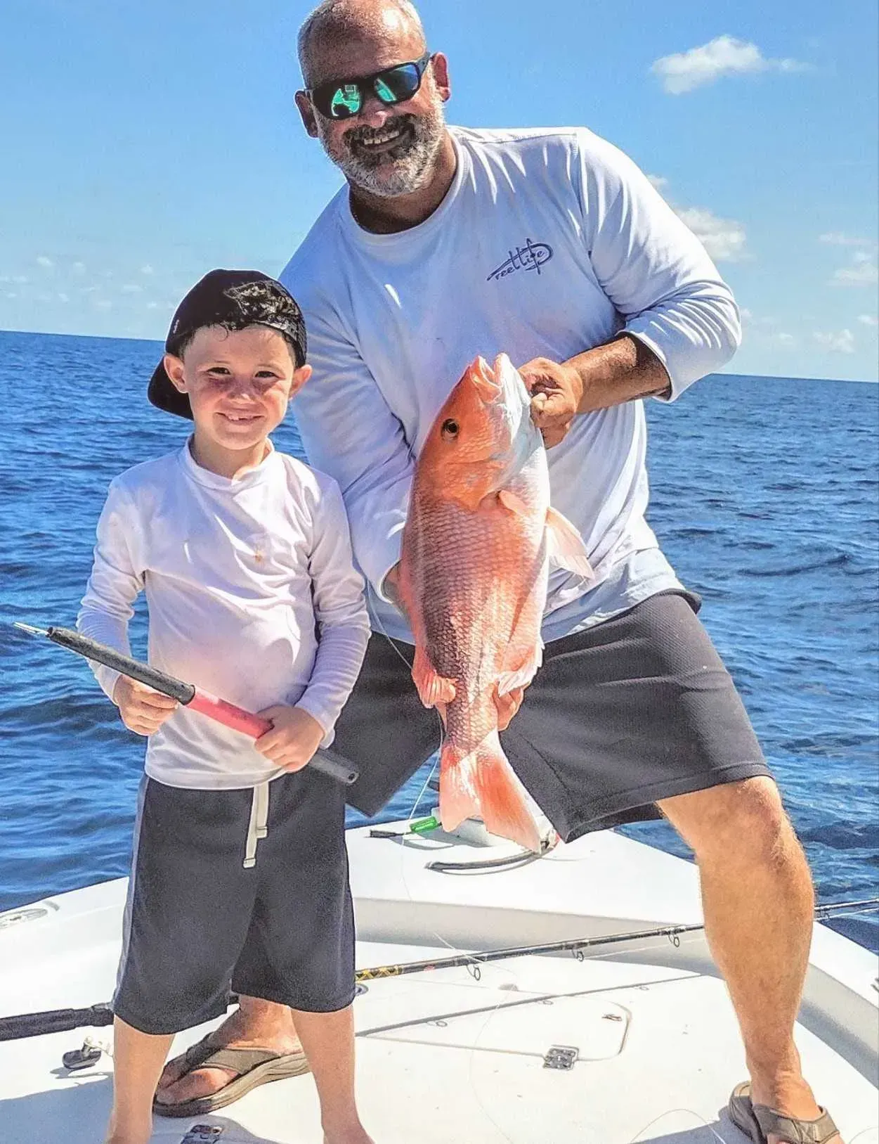 Two people on a boat holding a large fish against a bright blue ocean and sky.