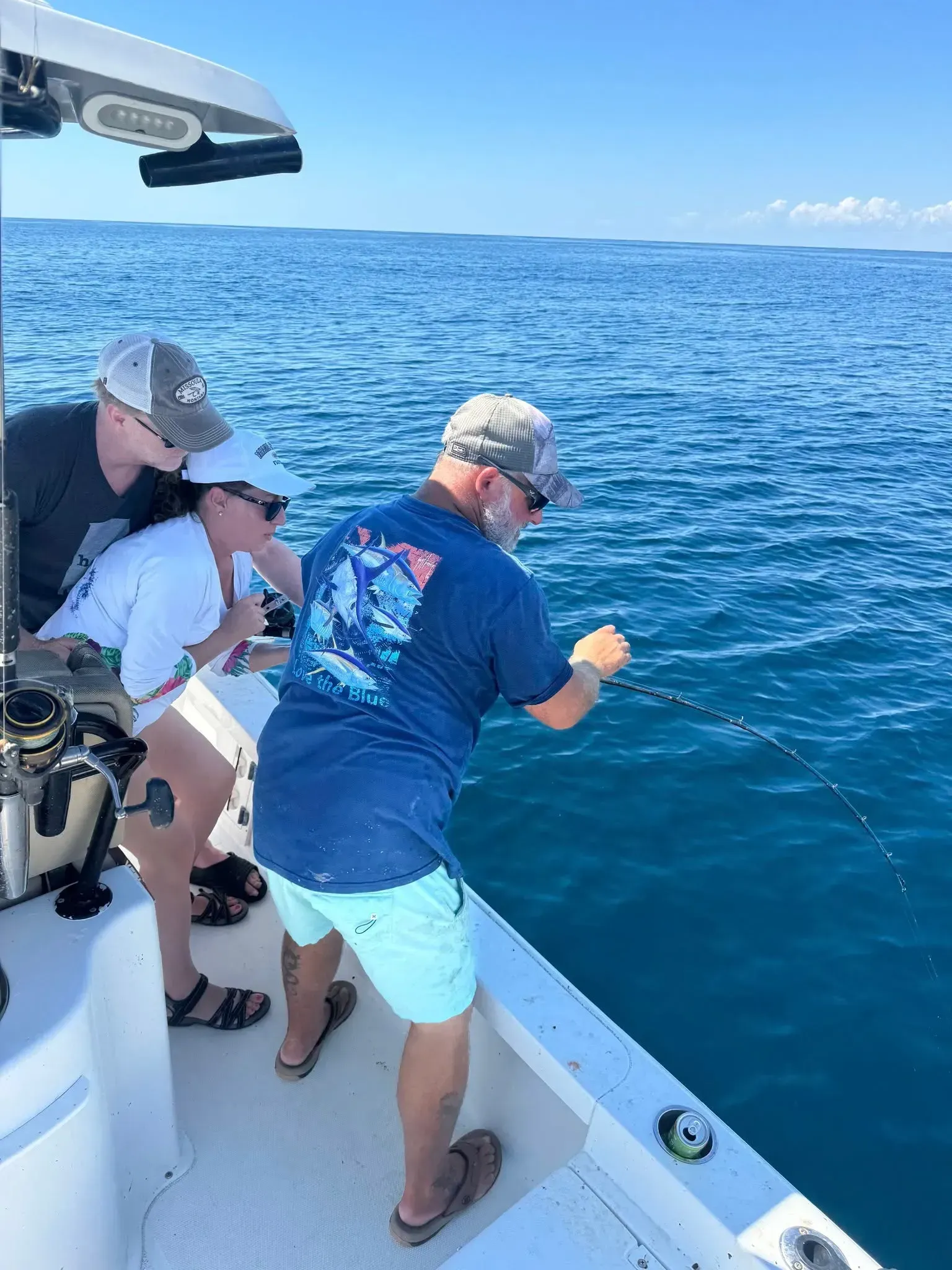 Two people fishing from a boat on a bright blue ocean under a clear sky