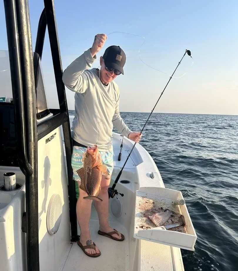Person on a boat holding a large fish over a cooler on the open water