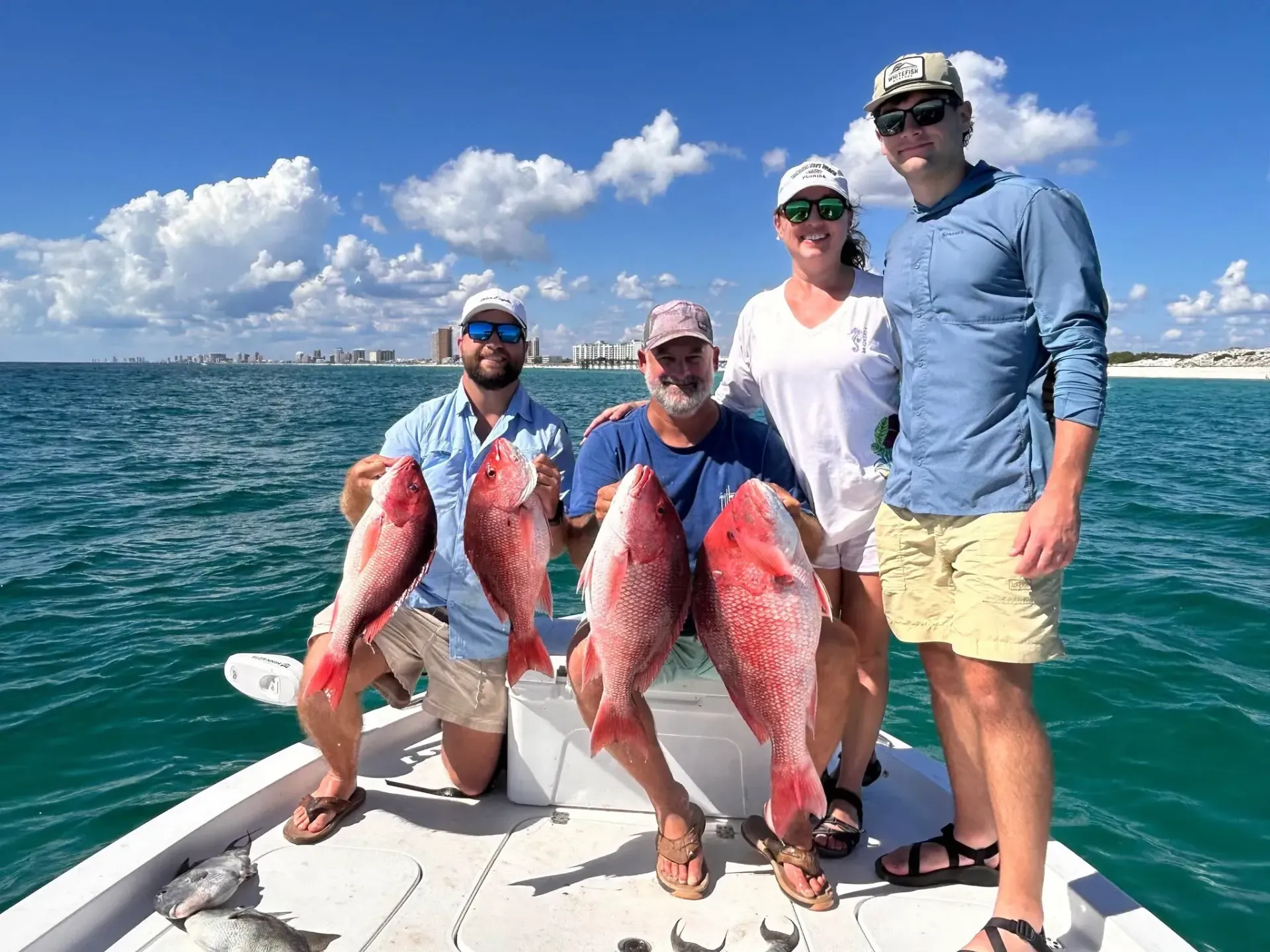 Four anglers on a boat hold two large red fish on a sunny ocean day.