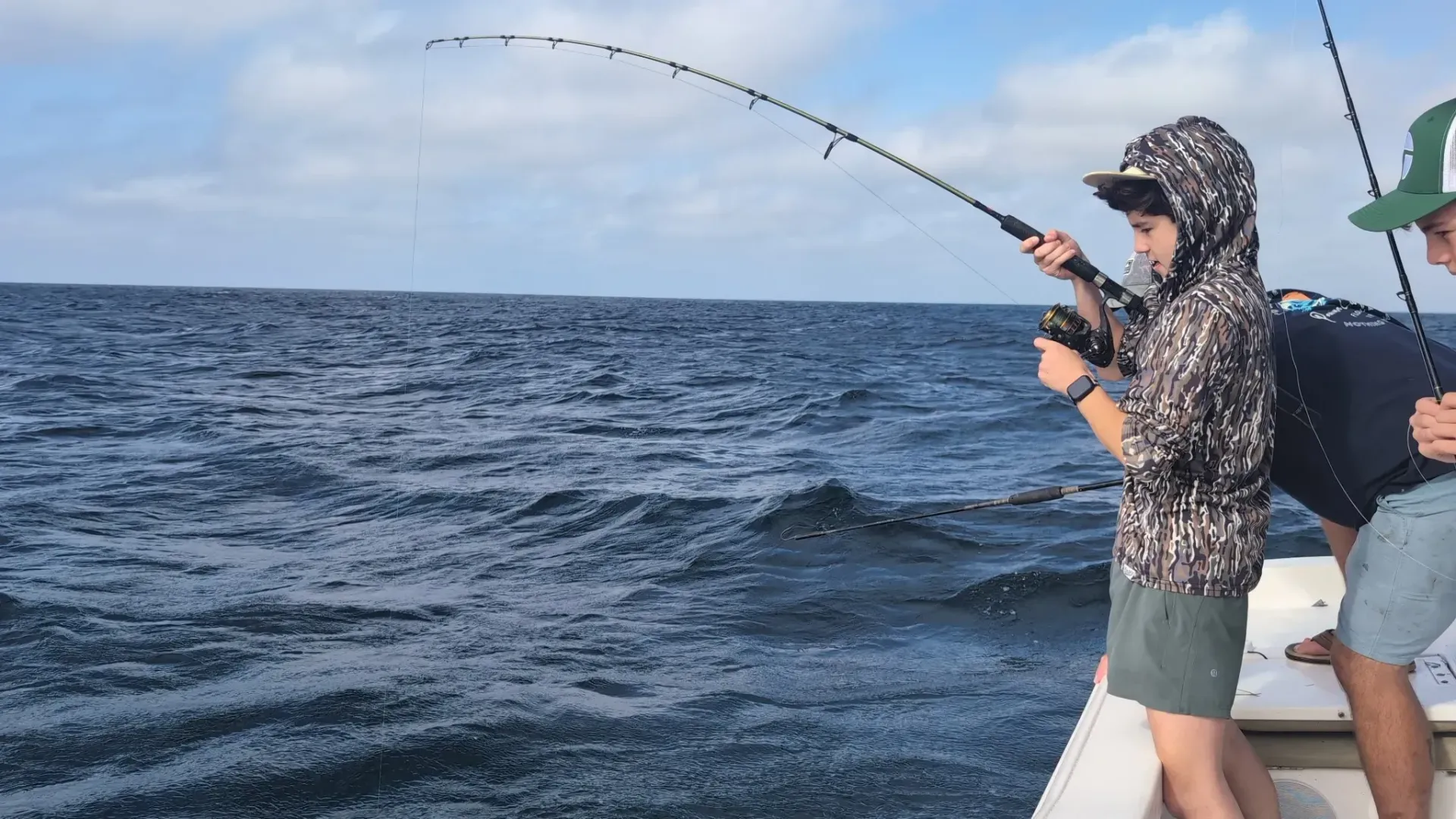 Person on a boat reels in a fishing rod over choppy blue water