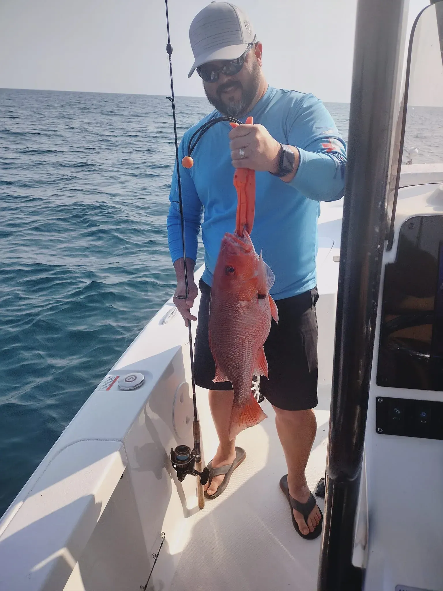 Man on a boat holding up a large red fish over open water