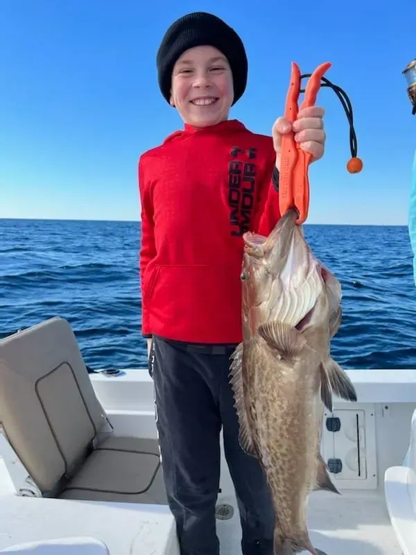 Person on a boat smiling and holding up a large fish against a blue ocean backdrop