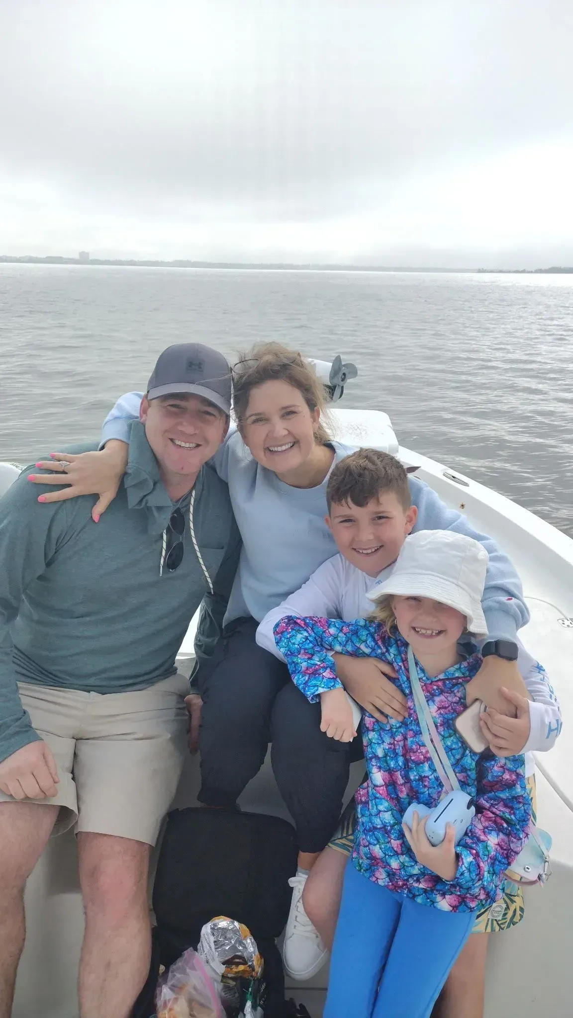 Four people smiling on a boat, with water and a cloudy shoreline in the background.
