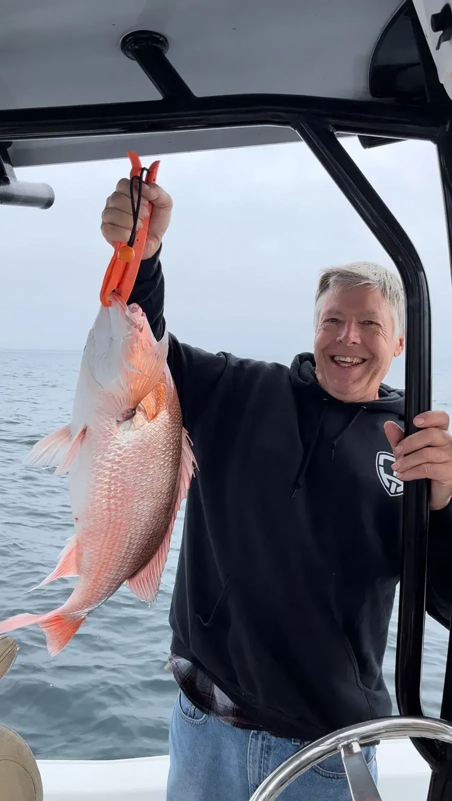 Smiling person on a boat holding up a large pink fish by the tail over the water