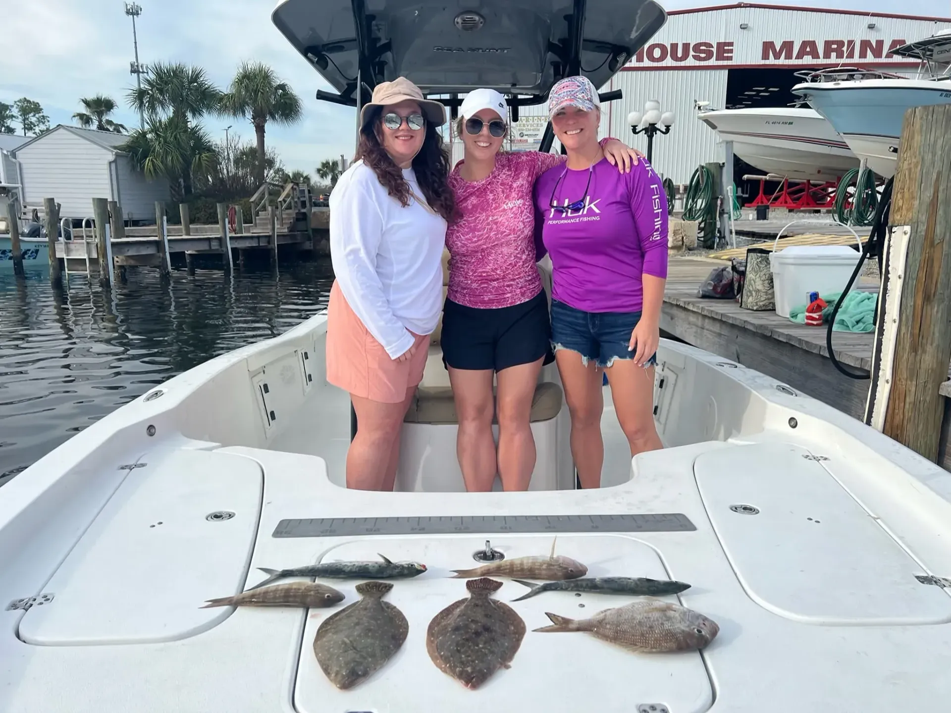 Three people posing on a fishing boat deck with several caught fish laid out in front of them.