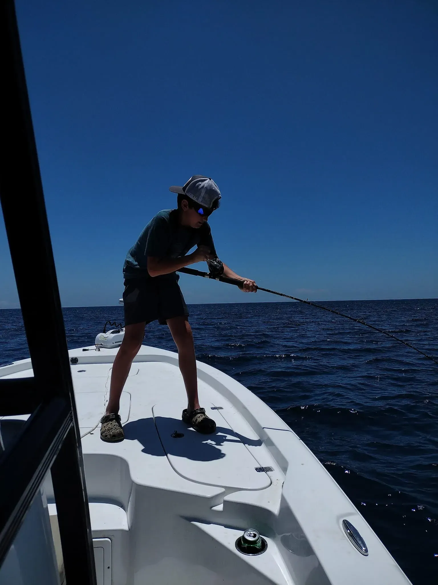 Person fishing from the bow of a boat on a sunny blue ocean.