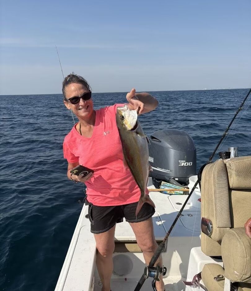 Person on a boat holding up a large fish on open water, wearing a pink shirt and sunglasses.